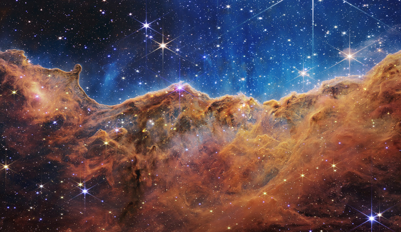 Captured in infrared light by NASA’s new James Webb Space Telescope, this image reveals for the first time previously invisible areas of star birth.  According to NASA, this image shows a landscape of “mountains” and “valleys” speckled with glittering stars, but is actually the edge of a nearby, young, star-forming region called NGC 3324 in the Carina Nebula.