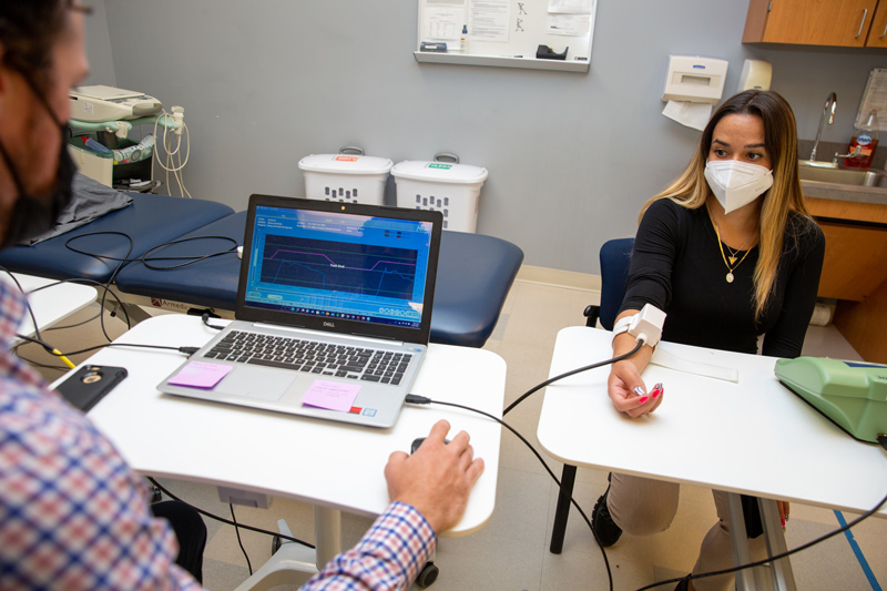 Ashley Fath, clinical research coordinator for UD’s Rehabilitation and Neuroplasticity Lab, wears a device that emits heat to induce pain as researchers seek to determine how sensitive someone might be to heat-based pain as part of a larger study on pain and motor learning. Graduate research assistant and doctoral student Patrick Knox (left) is analyzing pain levels on the screen. Ashley Fath, clinical research coordinator for UD’s Rehabilitation and Neuroplasticity Lab, wears a device that emits heat to induce pain as researchers seek to determine how sensitive someone might be to heat-based pain as part of a larger study on pain and motor learning. Graduate research assistant and doctoral student Patrick Knox (left) is analyzing pain levels on the screen.