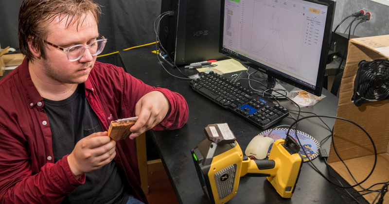 Wes Carson, an environmental chemistry major at the University of Delaware, uses a hand-held spectrometer to analyze samples of exotic hardwood species.