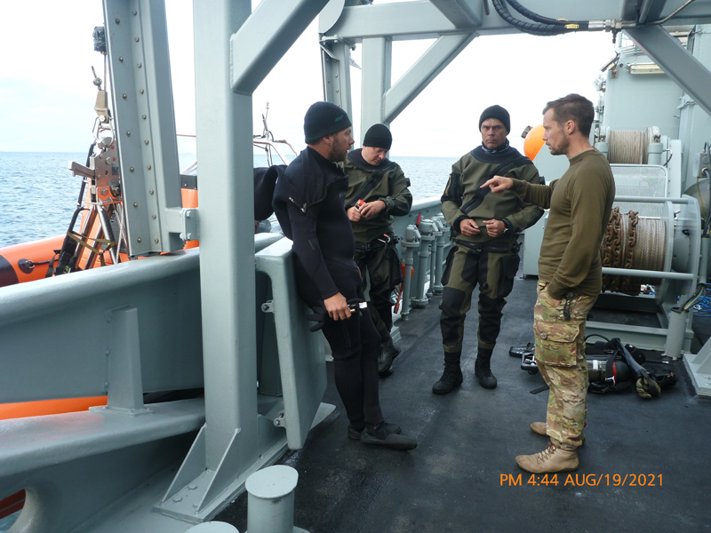 In early August of 2021, a joint effort between the University of Delaware, Project Recover, the Royal Danish Navy and the Defense POW/MIA Accounting Agency (DPAA), led to an underwater survey of two areas where the B-24s went down in an effort to account for those missing Airmen. Pictured here is the pre-dive planning and discussion with the Royal Danish Navy Explosive Ordnance Disposal (EOD) Fleet Diving Unit Clearance Divers aboard the Royal Danish Navy Vessel. From left to right Matthew Breece, Allan Rosenberg (RDN), Christian Gammeltoft (RDN), and Snorre Gudnason (RDN).