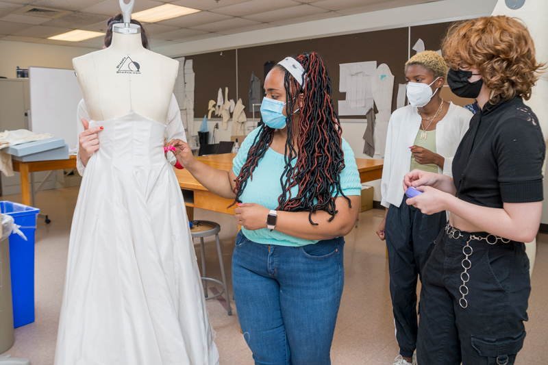 Students (from left) Kayla Brown, Maya Bordrick and Alex Culley study the way the gown will fall as Katya Roelse holds it on a mannequin in the Fashion and Apparel Studies workroom. Students (from left) Kayla Brown, Maya Bordrick and Alex Culley study the way the gown will fall as Katya Roelse holds it on a mannequin in the Fashion and Apparel Studies workroom.