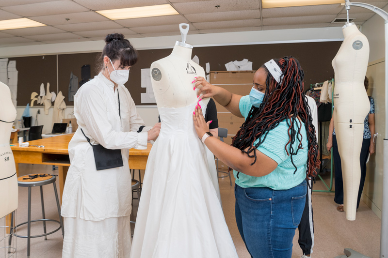 Katya Roelse and Kayla Brown fit the partially finished skirt on a mannequin. The gown has no waistline seam, another characteristic Ann Lowe design element.