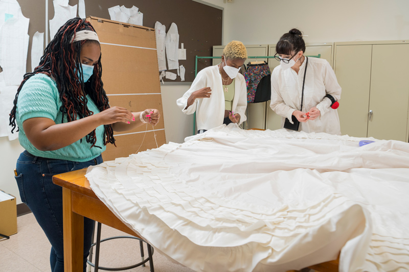 Sewing the tiers of ruffles onto the reproduction wedding gown are (from left) students Kayla Brown and Maya Bordrick and instructor Katya Roelse. The team used 154 yards of taffeta trim, basting and gathering it to make the ruffles.