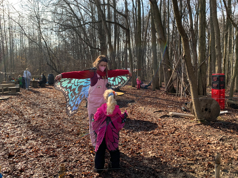 A preschooler learns about butterflies and nature with a University of Delaware student in the wooded area adjacent to the Lab School.