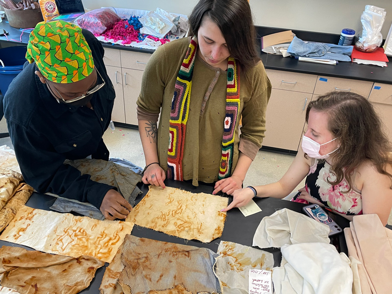 Students (from left) Diadem Abayode, Shae Woodruff and Michelle Yatvitskiy work on a project using waste metal to create designs on fabric colored by iron oxide.