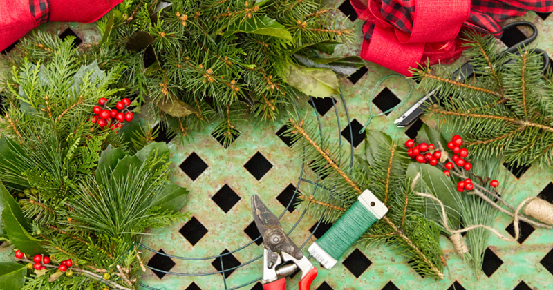Greenery, twine and tools for assembling a holiday wreath sit on a table