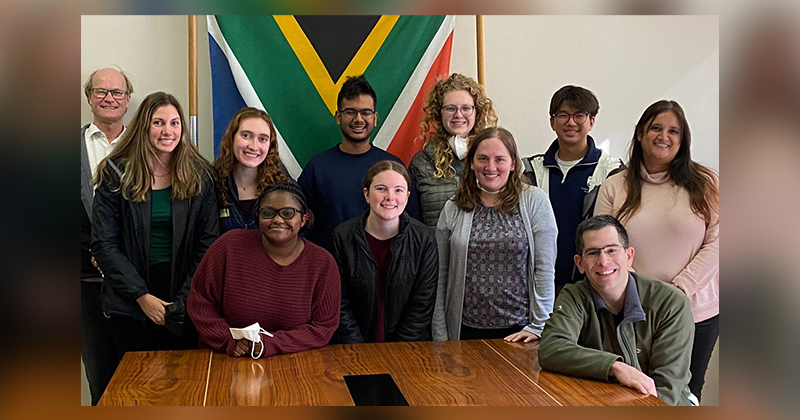 A team of students from the University of Delaware and the University of Pennsylvania, supported by Professor Julie Karand, join three clinicians they interviewed at a dental facility in Cape Town, South Africa. The country’s flag can be seen in the back.