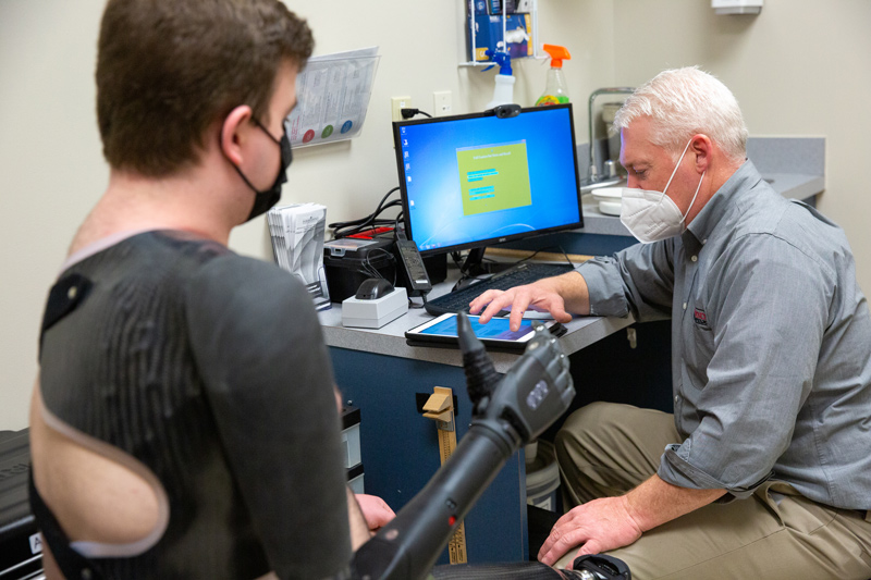 John Horne (right), president of Independence Prosthetics-Orthotics on UD’s STAR Campus, helps UD graduate Aidan Bradley program his bionic arm which uses pattern recognition technology to recognize movements and associate them with specific tasks.