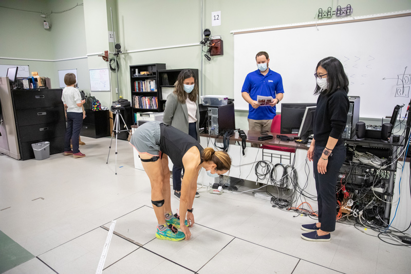 Study participant Jennifer Kraut stretches while wearing her newly outfitted sensors that will give biomechanics and movement science doctoral students (L to R) Mayumi Wagatsuma, Julien Mihy and Fany Alvarado, a glimpse into her everyday walking patterns. The research in Jocelyn Hafer’s Gait Biomechanics Research Lab will provide a wealth of data to explore how pain and fatigue impacts joint health. 