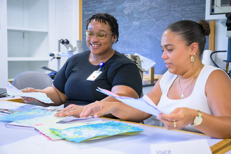 Gabrielle Hilliard (left) and Joyce G. Vázquez Villanueva look at samples of a paper marbling activity. 