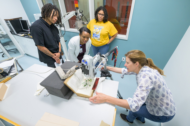 Dorian Henry, Dominique V. Goden and Sinclair Strong watch Catherine Matsen, senior scientist and affiliated associate professor, demonstrate a hand-held X-ray fluorescence machine, one of the many tools used in the Winterthur labs.