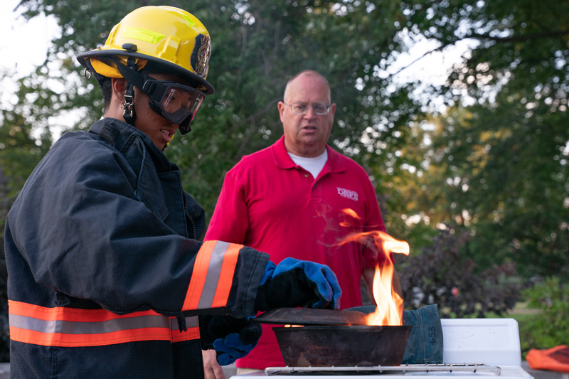 Paul Eichler, a representative from the Delaware State Fire School, instructs resident assistant Bryan Tiamson (left) on how to put out a stovetop fire with a pan lid.