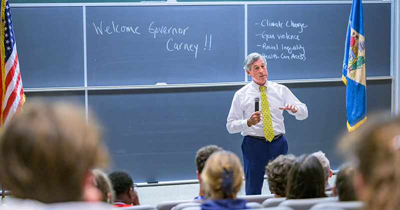 Delaware Gov. John Carney talks to students gathered in Kirkbride Lecture Hall for the Governor’s School for Excellence, held each year at UD. Topics of the day’s discussion can be seen on the blackboard behind the governor.
