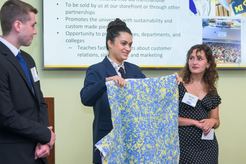Veepra Mishra, fashion designer, holds a sample fabric as she discusses some of the proposals of the DelaWEAR Spin In team. Kieran Singley (left), marketing specialist on the team, and Miranda Rack, merchandising planning specialist, listen.