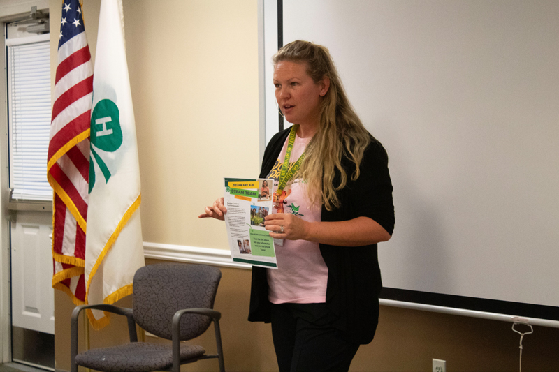 Twila Parish-Short holds the STEAM Team information flier and explains what the STEAM Team entails to a group of youth and adults sitting around her. 