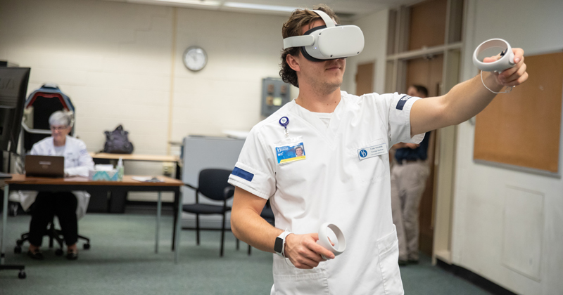 Senior honors nursing student Luke Stuchlik said he feels as though he’s been transported into a hospital room as he works to care for four patients as part of a new virtual reality simulation offering in the School of Nursing. Senior honors nursing student Luke Stuchlik said he feels as though he’s been transported into a hospital room as he works to care for four patients as part of a new virtual reality simulation offering in the School of Nursing.