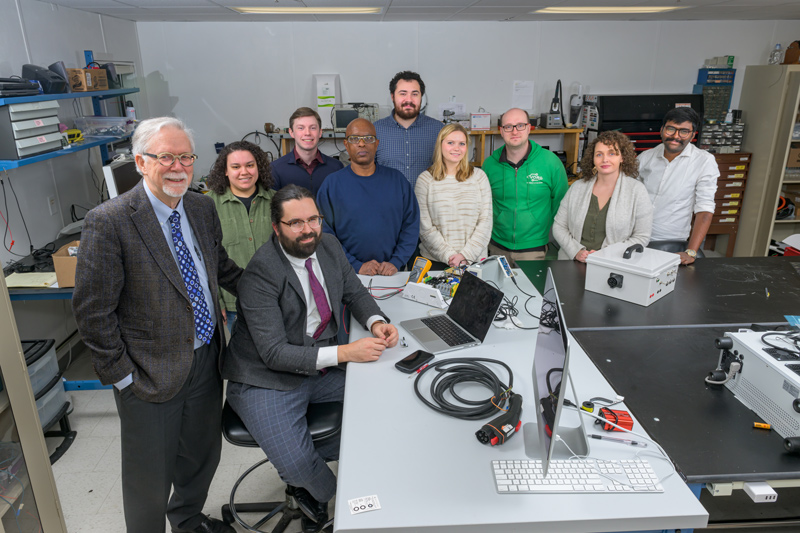 From left to right, Professor Willett Kempton with Rodney McGee (senior engineer, seated), and students and colleagues in their EV research lab at UD’s STAR Campus, including Marlene Toney, Samuel Ramos, Allen Mowbray, John Metz, Catherine Gilman, Garrett Ejzak (postdoc), Becky Cox (administrator) and Raman Kumar Rudraraju. 