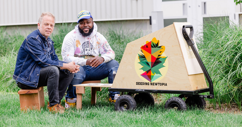 Aaron Terry, left, and Amir Campbell sit with the art cart they created for public events and story gathering.