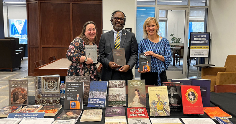 Julia Oestreich (left), director of the UD Press; Trevor A. Dawes (center), vice provost for libraries and museums and May Morris University Librarian; and Laura Carlson, UD provost, gathered at the centennial anniversary celebration of the UD Press in March 2023. They are holding and surrounded by a variety of titles published by the UD Press.
