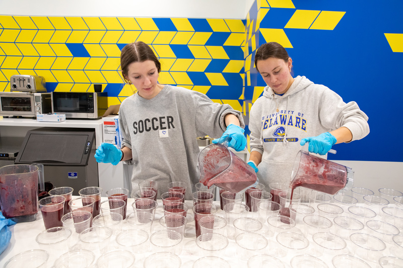 Smoothies on “Thirsty Thursday” are a fan favorite among UD’s student-athletes. Junior Ang Rann (left) and sophomore Lexi Harrison, who are interns in the UD Athletics’ performance nutrition program, are pouring the “Purple Power” smoothie, which gives athletes the carbs they need for endurance and high-intensity performance.