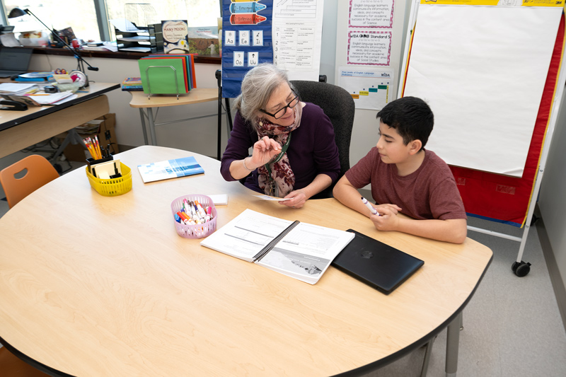 Teacher Maggi McNutt works with Nikolas, a sixth-grader newly arrived in the U.S., to help him develop his English language skills at Academia Antonia Alonso Charter School, a dual-language immersion school near Newark, Delaware. On this day, Nikolas is using a combination of technology (laptop) and hand-written index cards to learn the English words for math terms such as “fraction” and “reciprocal” that he will need in his mainstream classroom math lessons.