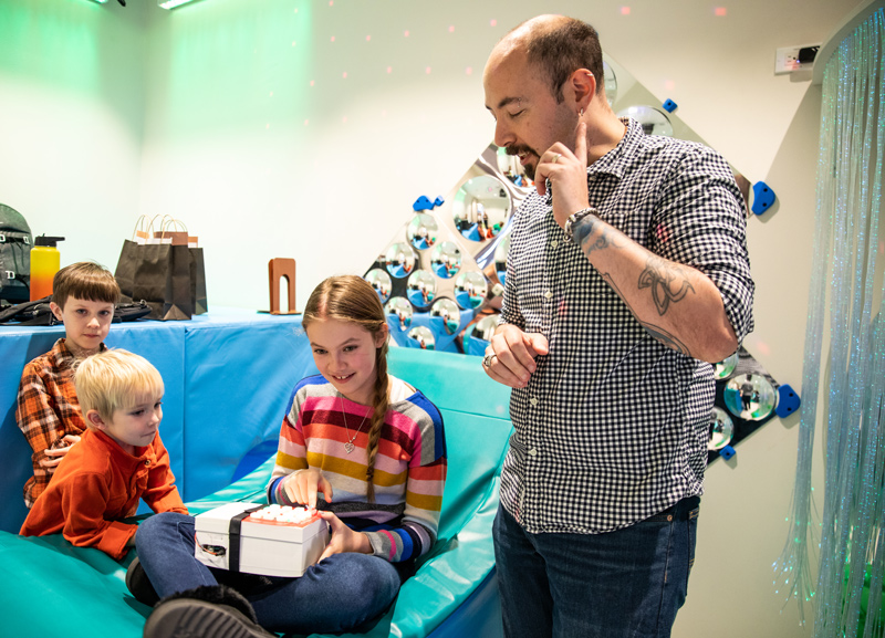 Matthew Mauriello, assistant professor of computer and information sciences, helped to design, build and deploy the technology used in the music listening device for children with autism.  He is pictured showing children how to use the device inside the Route 9 Library and Innovation Center.