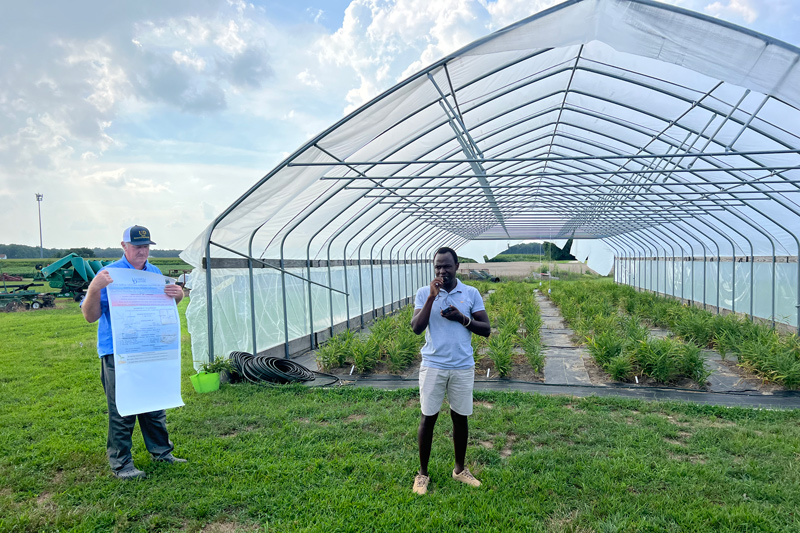 In 2022, Gordon Johnson holds a research poster while his graduate student Shem Elias presents his findings on growing baby ginger.