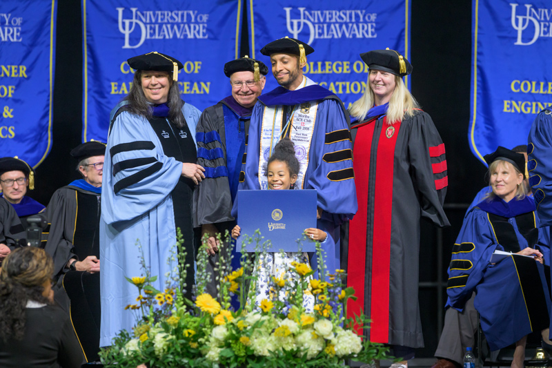 Chester Holland IV brought a special guest — six-year-old daughter, Adriana — with him to the platform to receive his doctoral hood in urban affairs and public policy. With him from left are Amy Ellen Schwartz, dean of the Joseph R. Biden Jr. School of Public Policy and Administration, Daniel Rich, professor emeritus of public policy, and his adviser, Sarah Bruch, associate professor and director of the doctoral program in urban affairs and public policy. 