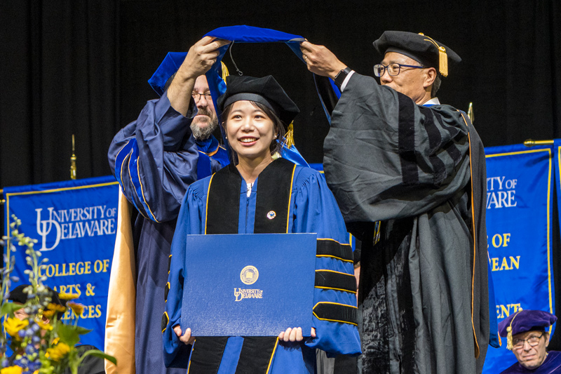  Xinyu Li receives the doctoral hood from Fabrice Veron (left), dean of the College of Earth Ocean and Environment, and her adviser, Wei-Jun Cai, the Mary A.S. Lighthipe Professor in the School of Marine Science and Policy.