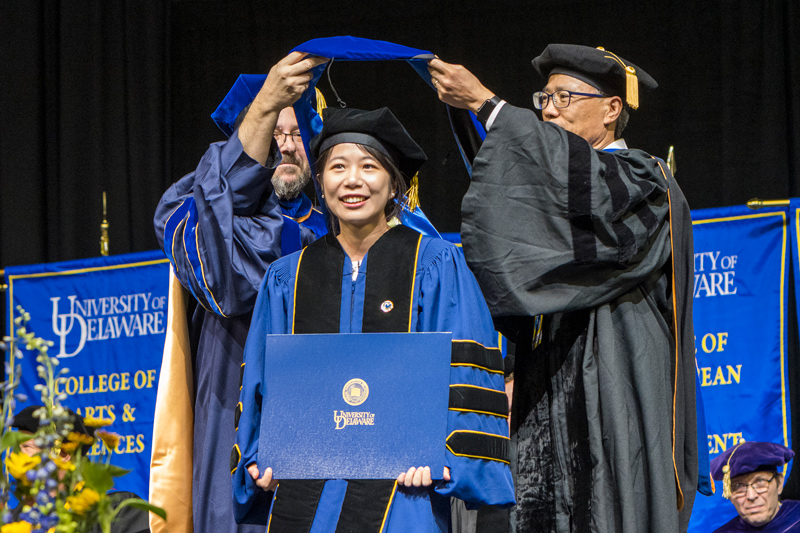 Xinyu Li receives the doctoral hood from Fabrice Veron (left), dean of the College of Earth Ocean and Environment, and her adviser, Wei-Jun Cai, the Mary A.S. Lighthipe Professor in the School of Marine Science and Policy. Xinyu Li receives the doctoral hood from Fabrice Veron (left), dean of the College of Earth Ocean and Environment, and her adviser, Wei-Jun Cai, the Mary A.S. Lighthipe Professor in the School of Marine Science and Policy.