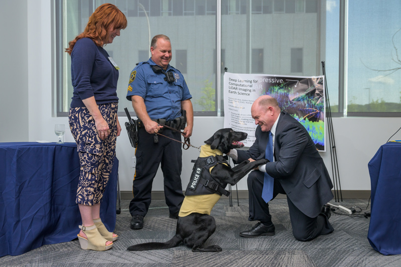 U.S. Sen. Chris Coons meets Jetta, a bomb-sniffing dog, with her handler, UD Police Corporal John Saville, and UD inventor Martha Hall, who designed Jetta’s Kevlar sweater to protect her from harm.