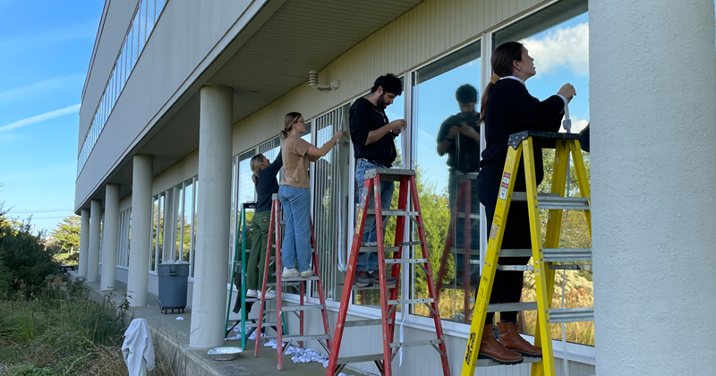 Students install circular-shaped decals on the windows of Cannon Laboratory on UD’s High R. Sharp Campus in Lewes