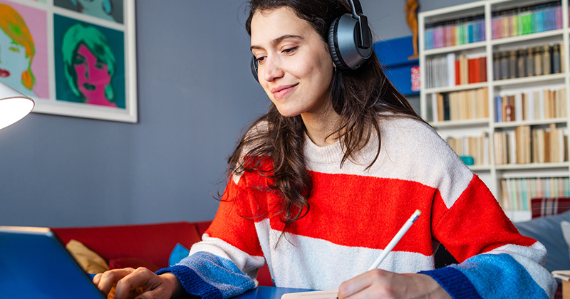Young woman with headphones on, sitting at a desk with a laptop.