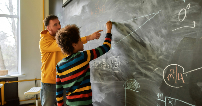 A student works with a teacher in a middle school mathematics classroom. 