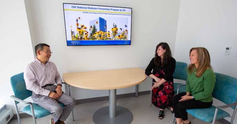 An image of three professionals sitting around a table in front of a TV screen