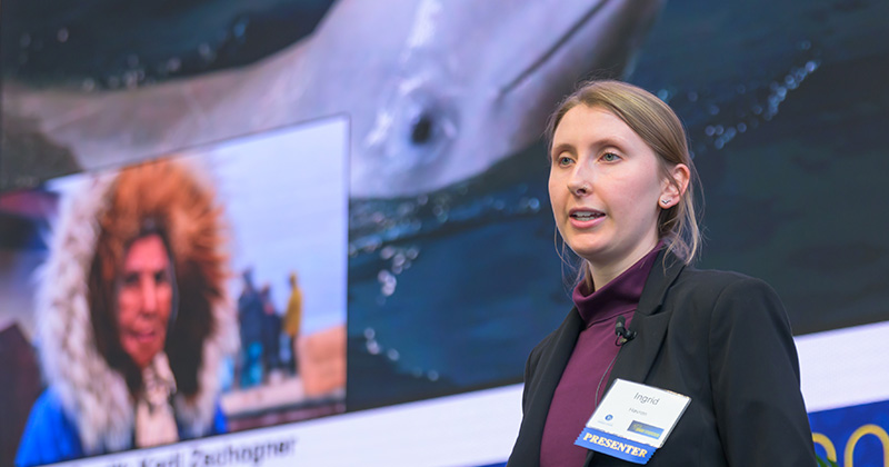 Presenter speaking in front of a large screen showing a whale