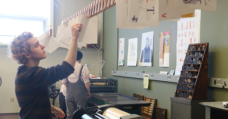 Rowan Dominick, who worked at Raven Press helping sort tiles, hangs newly printed cards to dry. 