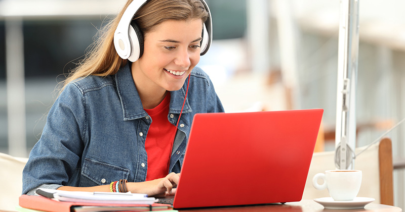 Young girl sitting at kitchen table, looking at laptop with headphones on