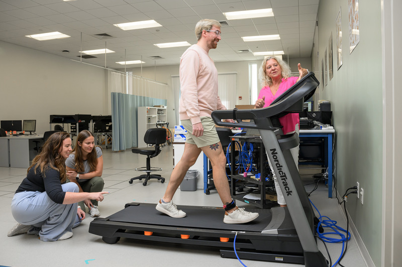 Andy Smith walks on a treadmill with a tensiometer around his right ankle. Stephanie Cone and Madeleine Krotine study his gait, while Karin Grävare Silbernagel monitors data collection.