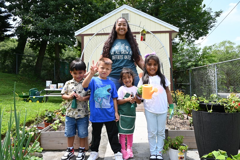 Diana Mercado, early childhood administrator at Pirulo’s Child Care and Learning Center, smiles with children in front of the garden she grew with the support of UD’s Let’s Grow Outside! initiative. 