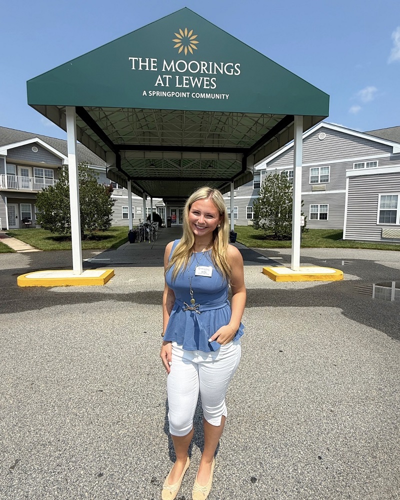 Lauria Tana-Dawson wears a blue shirt and white pants and poses in front of The Moorings in Lewes.