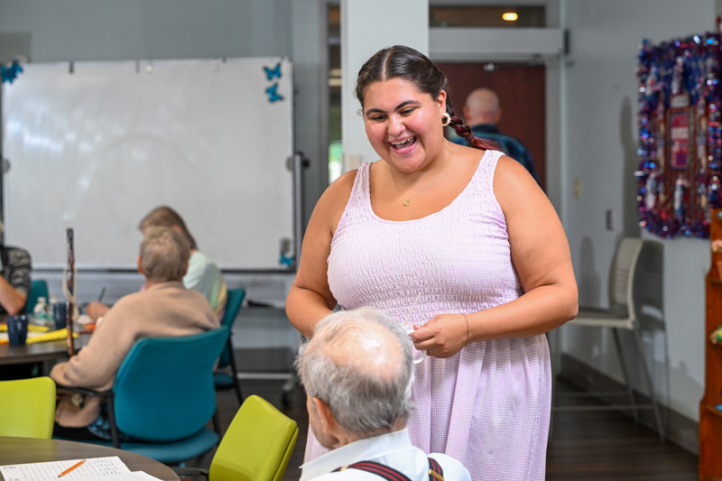 Grace DiGiacomo wears a purple dress and leads group activities at the Newark Senior Center