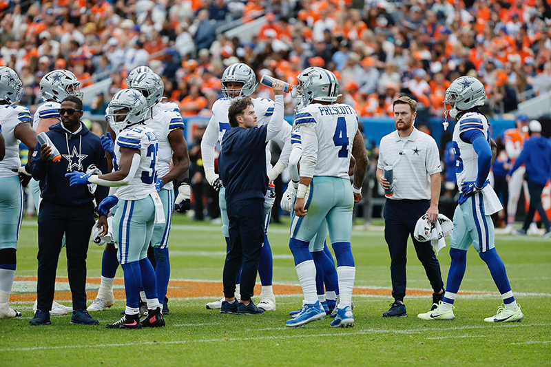 Blue Hen Nate Benjamin, a graduate assistant athletic trainer for the Dallas Cowboys, ensures quarterback Dak Prescott stays hydrated during a game time-out.  
