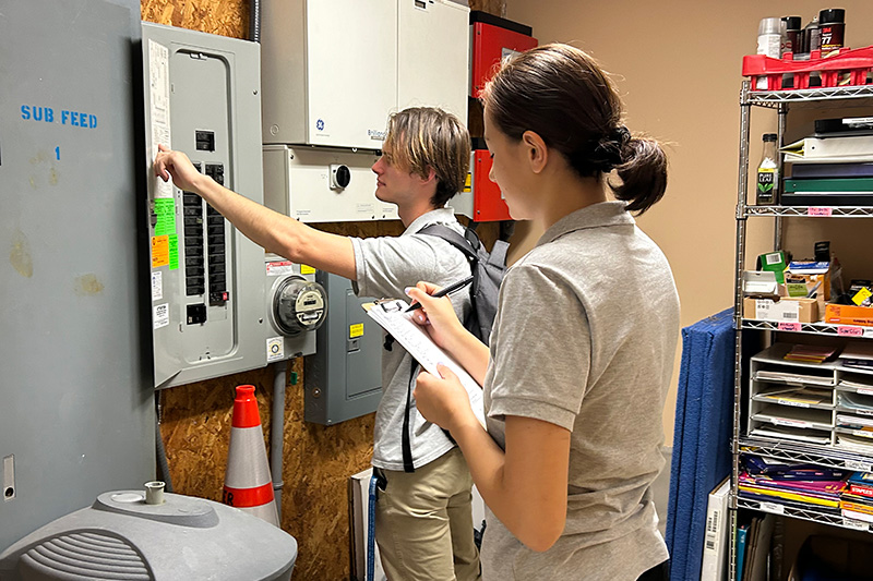 Eva Grise takes notes as Rocco Dumnich inspects an electrical panel. Auditors combine on-site observations with technical analysis to develop reports for clients.