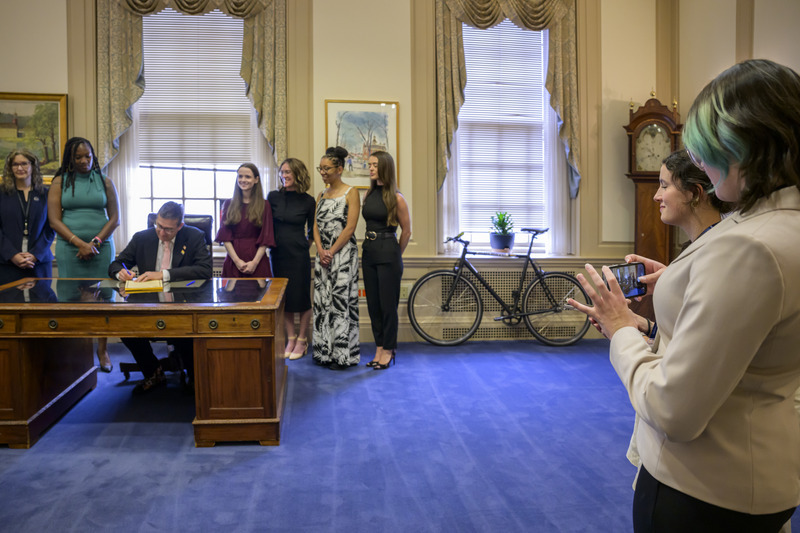Rohman and Hollinger watch as Gov. Meyer signed Senate Bill 250 into law. State Sen. Marie Pinkney (green dress) is the bill’s primary sponsor.