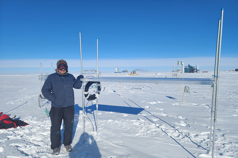 UD researcher Alexander "Sasha" Novikov installed new surface detectors at IceCube. He is at one of these detectors in this photo, taken in January 2025. The IceCube Lab can be seen in the background.