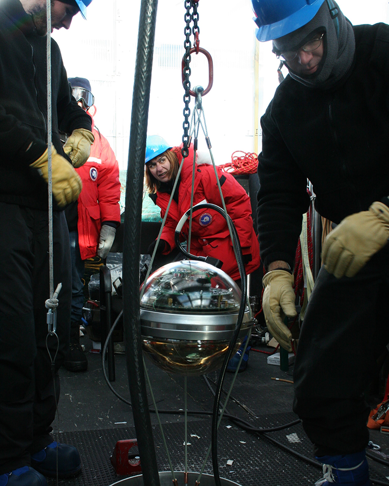 In this landmark photo, University of Delaware researcher Serap Tilav is deploying the first IceCube string in January of 2005, controlling the cable drop with a device in her hand. Another 85 strings and more than 5,000 sensors would be added in subsequent years.