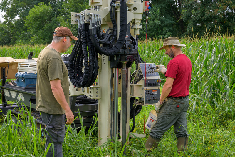 Lou Saporito (left) and Mike Reiner (right) guide a soil coring machine to collect soil samples from the ground. The researchers collected soil and root samples using a remote-controlled soil coring machine that hammered long tubes a meter into the ground. The soil cores helped validate the geophysical data. The Kernza soil was dark brown at the top of the tube, fading into a lighter orangey-brown further down. 