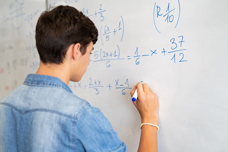A student completes an algebra problem at the whiteboard.