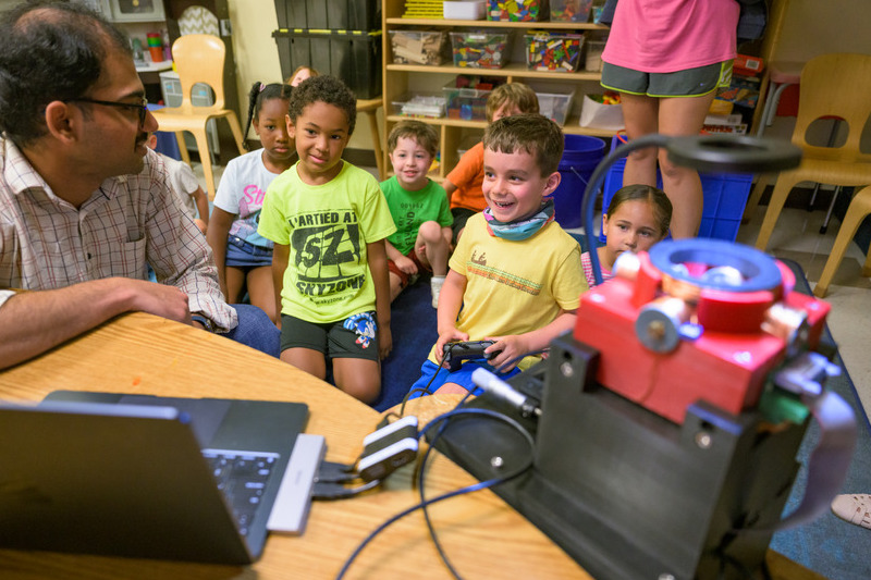 Cherukumilli talks with a student as he controls the microrobots. Starting with something familiar, such as a video game controller, helped the researchers explain the unfamiliar world of microrobotics to young children.